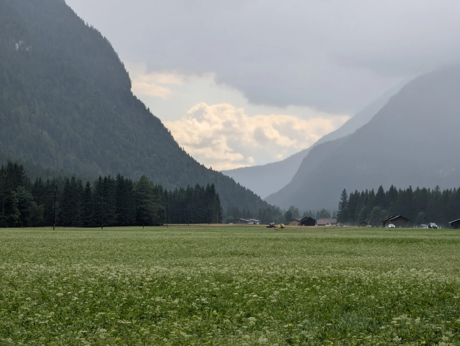 Mountain valley with haymaking in front of cloud-wrapped peaks