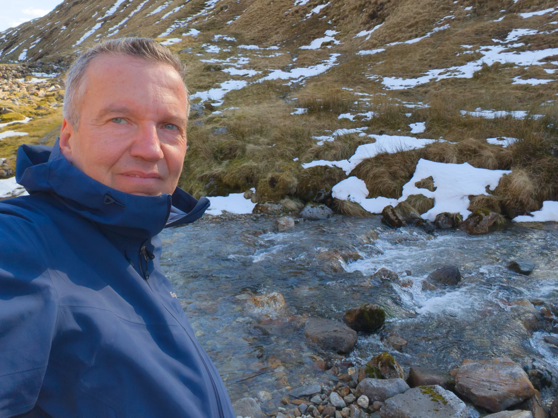 A short break by the burn — snow on the slope above