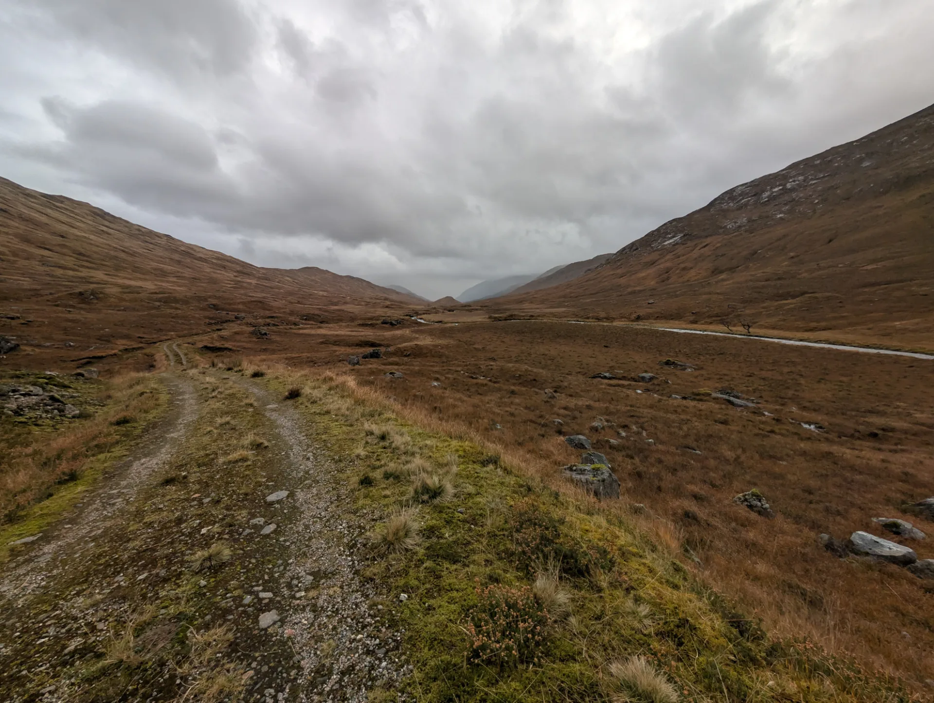 Stony path in the open valley, heavy cloud over the mountains